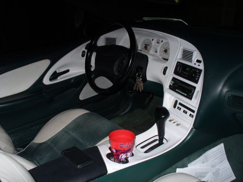 1995 Ford Thunderbird - Interior of a sports coupe with white and green two-tone trim, aftermarket stereo, automatic shifter and a red cup in the holder.