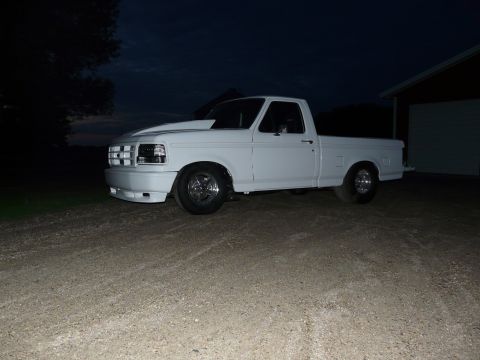 1994 Ford F-150 - Three-quarter front view of a white regular-cab short-bed Ford pickup on gravel at dusk beside a shed, lit against a dark blue sky. It has…