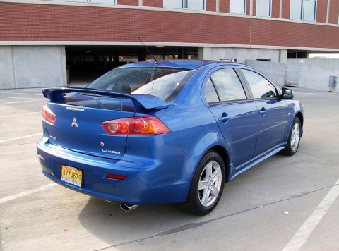 2009 Mitsubishi Lancer - This blue sedan has a spoiler and a distinctive rear design, suggesting a model year around 2008.