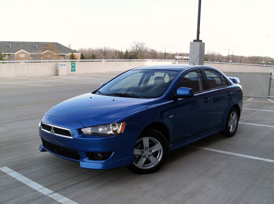 Blue Mitsubishi Lancer sedan on a parking garage rooftop, front three-quarter view