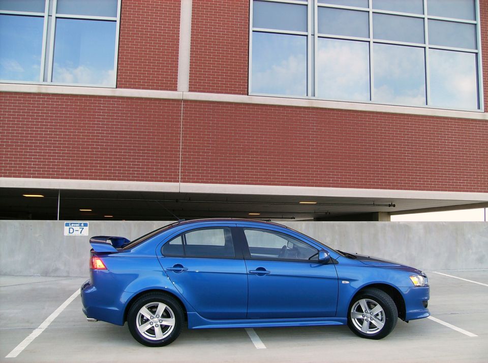 Blue Mitsubishi Lancer sedan side profile with rear spoiler on a parking garage deck
