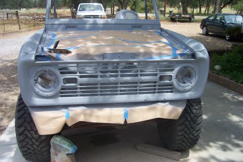 1976 Ford Bronco - A gray 1976 Ford Bronco is prepped for new paint, with its hood taped off and large off-road tires visible.