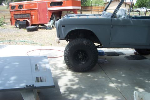 1976 Ford Bronco - SUV body in primer, with large off-road tires, parked outdoors next to a horse trailer.