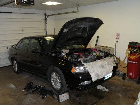 1998 Subaru Legacy - Black 1998 Subaru Legacy sedan with its hood open, revealing the engine bay while parked in a garage.
