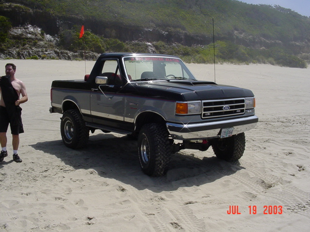 Ford Bronco parked on a sandy beach with a man standing nearby