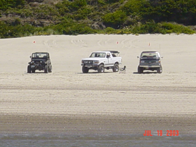 Black Jeep Wrangler and two white lifted 4x4 trucks parked on sand dunes, dated July 2003