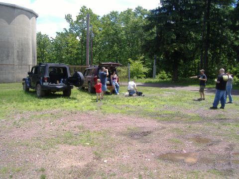 1988 Ford Bronco - People gather around two SUVs in an open field near trees and a large concrete structure.