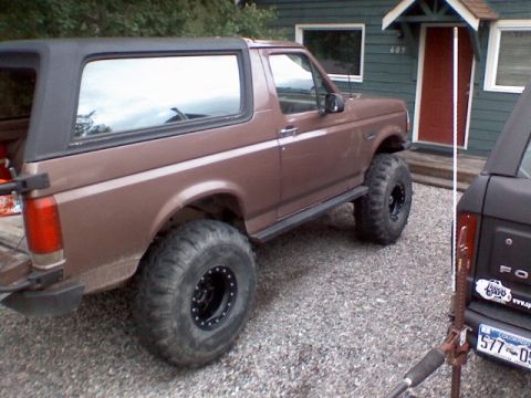 1993 Ford Bronco - Brown 1993 Ford Bronco with lifted suspension and large tires parked on gravel.