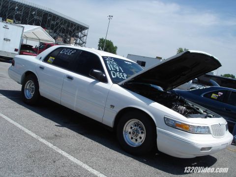 1998 Ford Crown Victoria - A white sedan sits with its hood open, possibly at a drag strip, with racing information visible on the windshield.