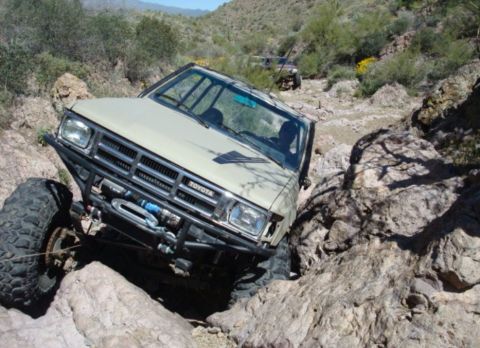 1986 Toyota Hilux - A modified Toyota pickup navigates a challenging rocky off-road course with another vehicle in the background.