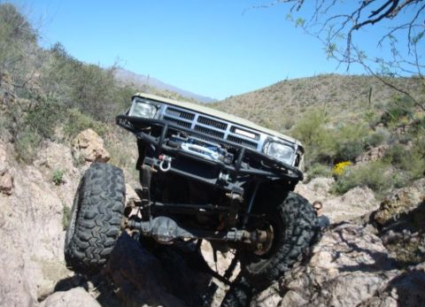 1986 Toyota Hilux - This modified truck is tackling a challenging rocky terrain under a clear blue sky.
