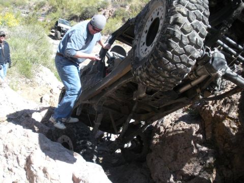 1986 Toyota Hilux - An off-road vehicle is stuck in a rocky ravine, with a person attempting to free it. Another vehicle is visible in the background.