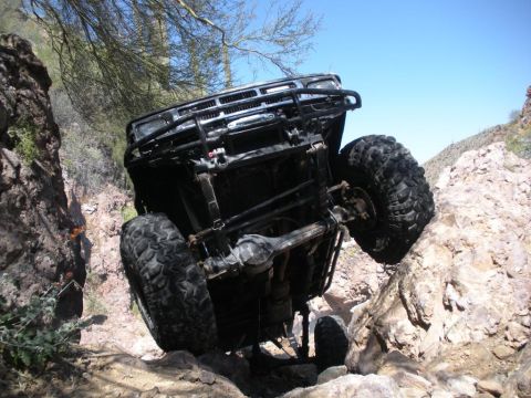 1986 Toyota Hilux - A black off-road truck is stuck on a rocky incline, tilted precariously.