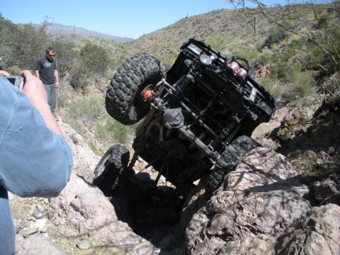 1986 Toyota Hilux - An off-road vehicle is stuck on a rocky incline, with a person filming the scene.