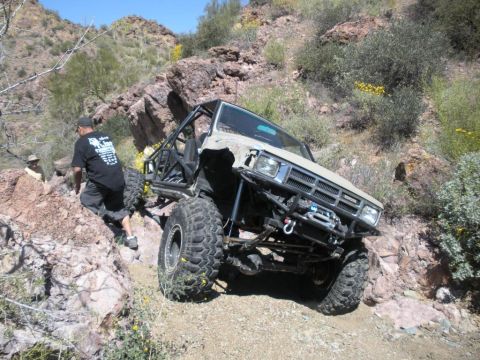 1986 Toyota Hilux - This heavily modified pickup truck is navigating a steep, rocky incline in a desert environment.