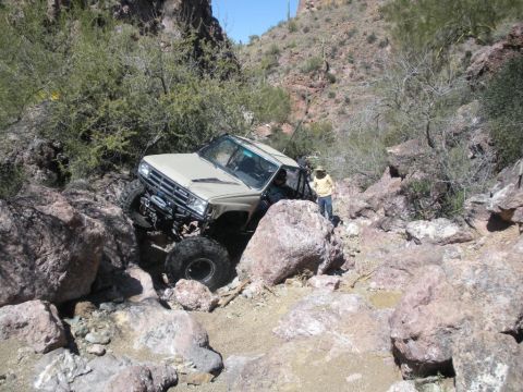 1986 Toyota Hilux - A modified tan truck navigates a challenging rocky trail in a desert canyon.