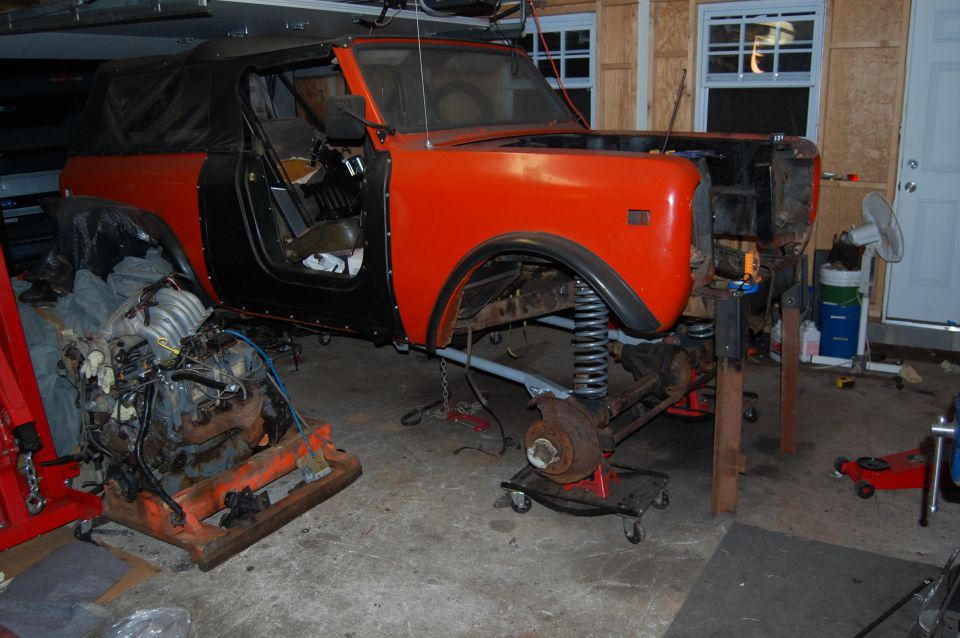 International Scout II body, disassembled, with engine removed and placed on an orange stand. Front suspension is exposed