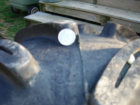 2008 Bombardier Outlander - A coin rests on the aggressive tread pattern of a large tire, with wooden steps visible behind.