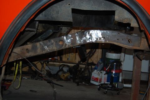 1994 Ford Bronco - The underside of a vehicle shows a heavily rusted frame and wheel well area, with various items stored in the background.