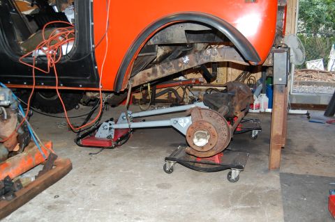 1994 Ford Bronco - The front suspension of an orange SUV has been removed and is supported by dollies in a garage setting.