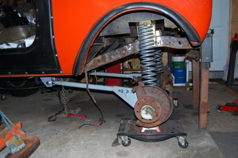 1994 Ford Bronco - Close-up view of the front suspension and brake assembly of an orange vehicle undergoing work.