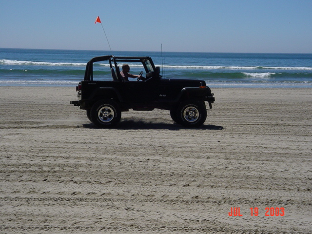 Black 1995 Jeep Wrangler driving on a beach
