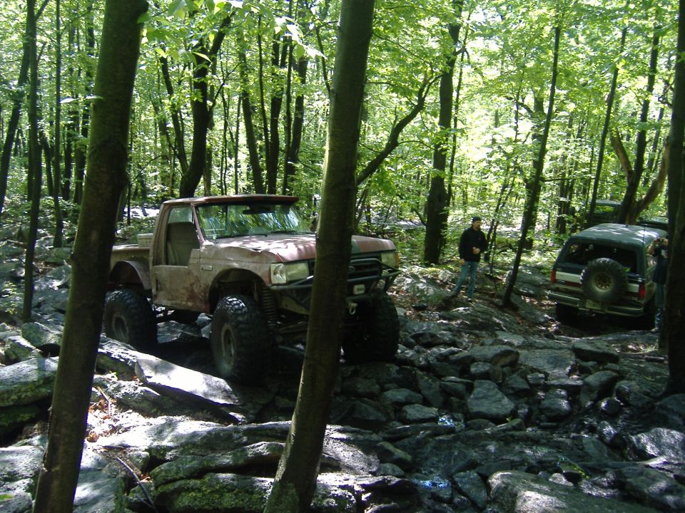 1988 Ford Bronco modified for off-roading on a rocky trail with another SUV behind it