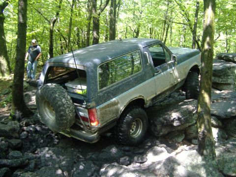 1988 Ford Bronco - A Ford Bronco navigates a rocky obstacle course in a forest setting.