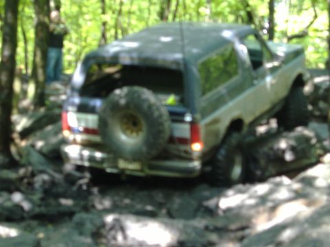 1988 Ford Bronco - A Ford Bronco navigates a rocky trail in a wooded area.