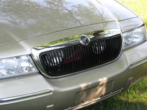 2000 Mercury Grand Marquis - Close-up of the front grille and headlights of a gold car, likely a 2000 Mercury Grand Marquis.
