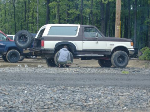 1988 Ford Bronco - Two people work on the rear tire of a 1988 Ford Bronco parked next to another vehicle.