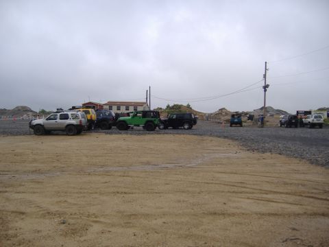 1988 Ford Bronco - Multiple off-road vehicles are parked in a gravel lot under an overcast sky.