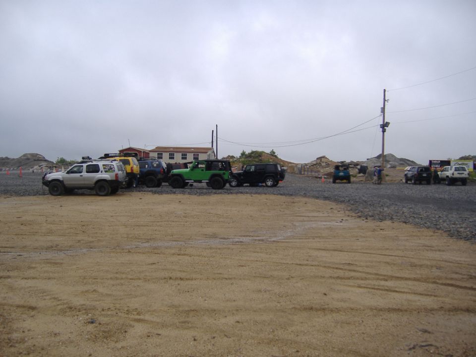 Several SUVs and Jeeps parked in an outdoor lot with buildings and rocky terrain in the background