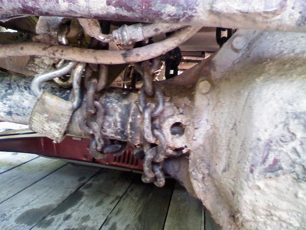Undercarriage of a dirty vehicle with chains wrapped around a differential and suspension components