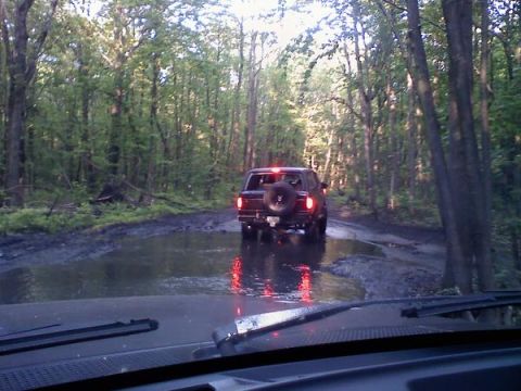 1988 Ford Bronco - A 1988 Ford Bronco navigates a water-filled, muddy path in a wooded area.