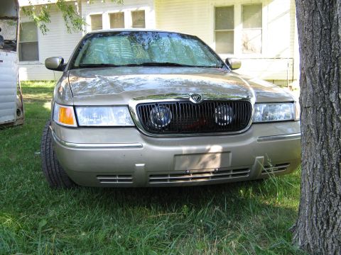 2000 Mercury Grand Marquis - A gold Mercury Grand Marquis is parked in front of a house, with a tree to its right.