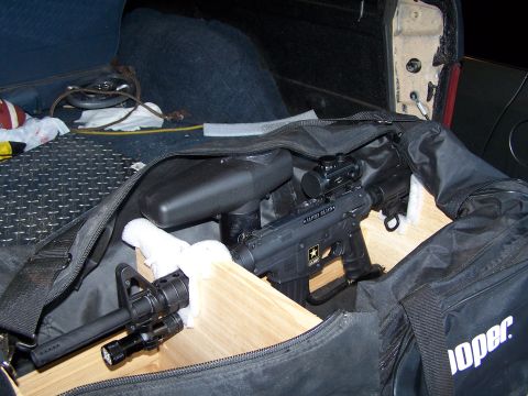 1986 Ford Bronco - A tactical paintball gun and accessories are stored in a duffel bag within the cargo area of a vehicle.