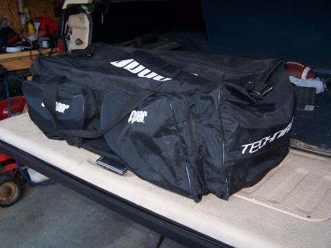 1986 Ford Bronco - A large black duffel bag with white lettering is placed inside a vehicle's cargo area.