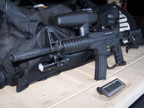 1986 Ford Bronco - A tactical-style paintball marker is shown with accessories, resting on a textured surface.