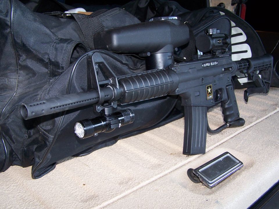 Paintball gun with hopper, flashlight, and scope, next to a duffel bag