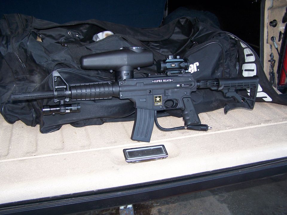 Black paintball gun with "ALPHA BLACK" text and US Army logo, resting on a black bag