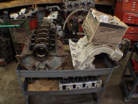 1996 Ford Bronco - Engine components, including a block, manifold, and head, are organized on a cart in a workshop.