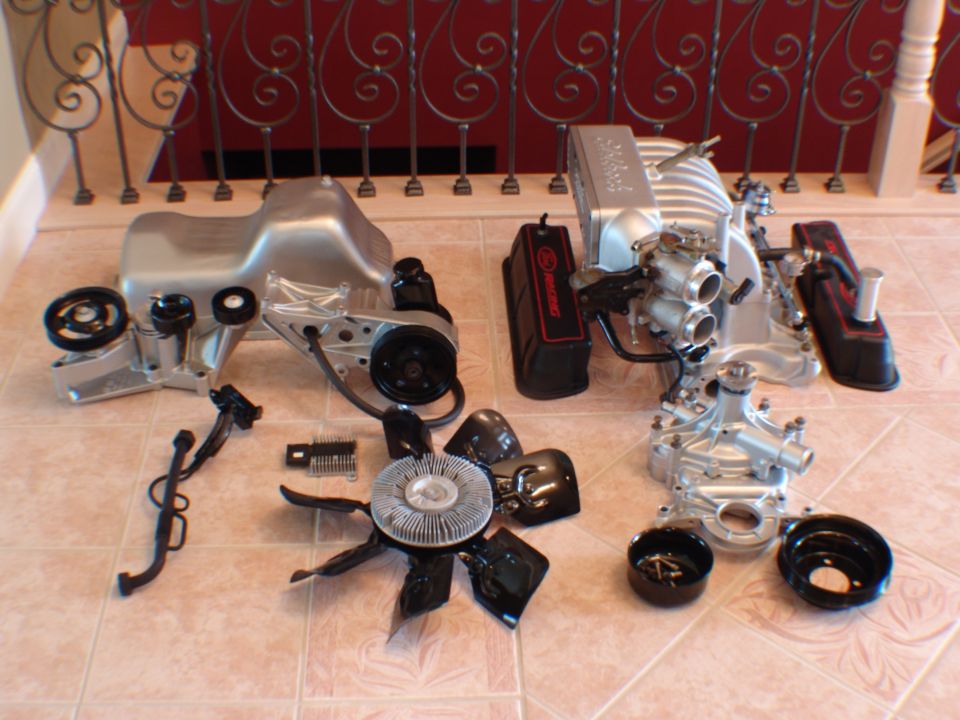 Engine parts including oil pan, intake manifold, valve covers, water pump, and fan laid out on a tiled floor