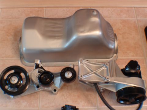1996 Ford Bronco - Engine parts including an oil pan and accessory bracket are laid out on a tiled surface.