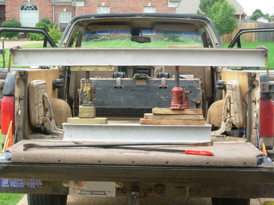 Despite the progress I made with the first pull, I decided to reset & use another jack.  This time, I'm bending the crossmember OUTboard of the body mounts, which should give me plenty of clearance between the t/g & frame later.

I'm also using the prybars between the bumper & body to pull out the dimples where the body mounts pushed into the bottom of the channel.  On the R, the lower tire carrier bracket is strong enough to use.  But on the L, I had to use a wood block with a steel plate directly under the crossmember.  The narrow Gorilla bar was the perfect size to fit into the gap.  The 36" Snap-On prybar wasn't long enough.