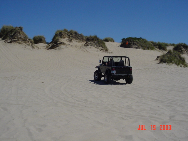 Topless tan Jeep Wrangler YJ with whip flag parked on sand dunes, 2003 date stamp