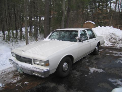 2001 Ford Crown Victoria - This white sedan, likely from the 1980s, is parked in a snowy area with trees in the background.