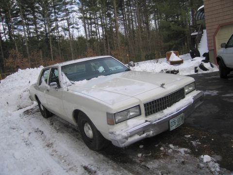 2001 Ford Crown Victoria - A white sedan sits in a snow-covered driveway, its front end partially obscured by snow.