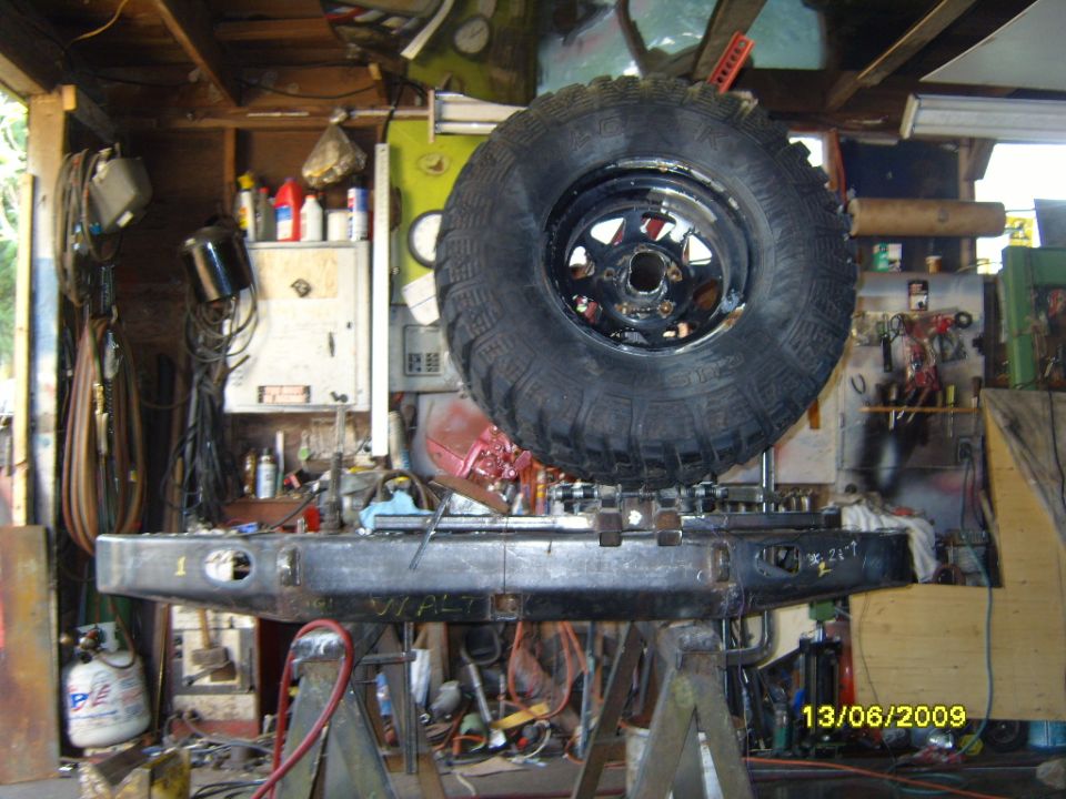 Spare tire mounted above a custom off-road bumper on jack stands in a garage