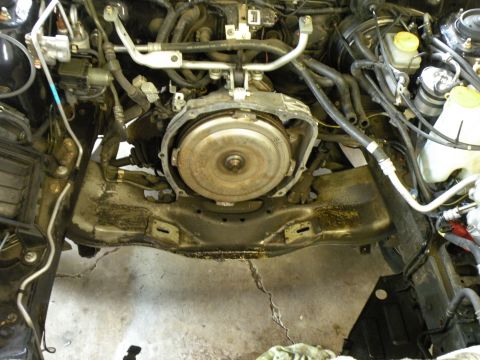 1998 Subaru Legacy - Engine bay of a 1998 Subaru Legacy with the transmission removed, revealing the torque converter and subframe components.